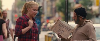 Movie still from “Trainwreck” (2015), directed by Judd Apatow – A woman holding up a cardboard sign on the side of the street; Medium shot, Low angle