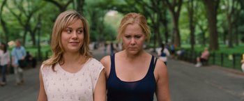Movie still from “Trainwreck” (2015), directed by Judd Apatow – Two young women standing next to each other in a park; Close Up shot, Over the shoulder angle