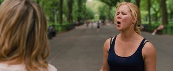 Movie still from “Trainwreck” (2015), directed by Judd Apatow – A woman standing on the side of a road with trees in the background; Medium shot, Over the shoulder angle