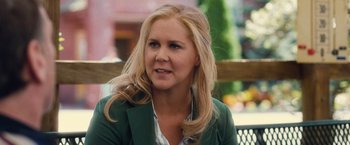 Movie still from “Trainwreck” (2015), directed by Judd Apatow – A woman with blonde hair sitting on top of a wooden bench; Close Up shot, Over the shoulder angle