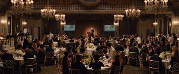 Movie still from “Trainwreck” (2015), directed by Judd Apatow – A group of people sitting at tables in front of a microphone; Extreme Wide shot, High angle