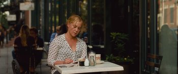 Movie still from “Trainwreck” (2015), directed by Judd Apatow – A woman sitting at an outdoor table with a cup of coffee; Medium shot, High angle