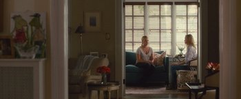 Movie still from “Trainwreck” (2015), directed by Judd Apatow – A woman sitting on top of a blue couch in a living room; Wide shot, Over the shoulder angle