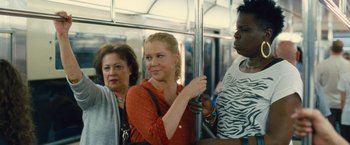 Movie still from “Trainwreck” (2015), directed by Judd Apatow – A woman standing next to two other people on a bus; Medium shot, Over the shoulder angle