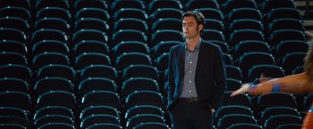 Movie still from “Trainwreck” (2015), directed by Judd Apatow – A man standing in front of rows of chairs; Medium shot, High angle