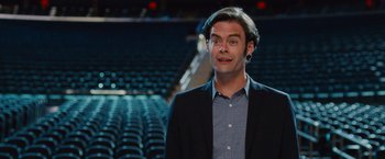Movie still from “Trainwreck” (2015), directed by Judd Apatow – A man standing in an empty stadium with rows of seats behind him; Close Up shot, Over the shoulder angle