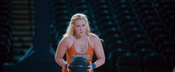 Movie still from “Trainwreck” (2015), directed by Judd Apatow – A woman holding a basketball in front of an audience; Medium shot, Over the shoulder angle