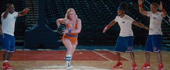 Movie still from “Trainwreck” (2015), directed by Judd Apatow – A female basketball player in an orange and blue uniform; Wide shot, Over the shoulder angle