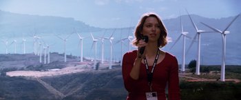 Movie still from “Transcendence” (2014), directed by Wally Pfister – A woman holding a microphone in front of wind turbines; Medium shot, Low angle