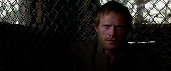 Movie still from “Transcendence” (2014), directed by Wally Pfister – A person with a chain link fence; Close Up shot, Over the shoulder angle