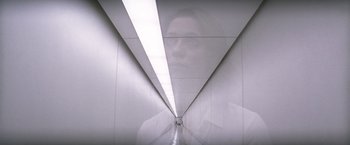 Movie still from “Transcendence” (2014), directed by Wally Pfister – A woman is reflected in a mirror in a hallway; Medium shot, Low angle