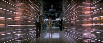 Movie still from “Transcendence” (2014), directed by Wally Pfister – Three people are standing in an illuminated hallway; Wide shot, Low angle