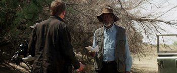Movie still from “Transcendence” (2014), directed by Wally Pfister – A man wearing a hat talking to another man in front of a tree; Medium shot, Over the shoulder angle