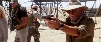 Movie still from “Transcendence” (2014), directed by Wally Pfister – A man holding a cell phone while standing next to another man; Medium shot, Over the shoulder angle