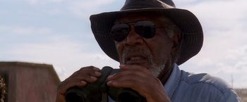 Movie still from “Transcendence” (2014), directed by Wally Pfister – An older man wearing a hat and sunglasses looking through a pair of binoculars; Close Up shot, Low angle