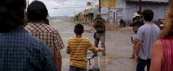 Movie still from “Transcendence” (2014), directed by Wally Pfister – A police officer taking a picture of a boy riding a bike; Wide shot, Over the shoulder angle