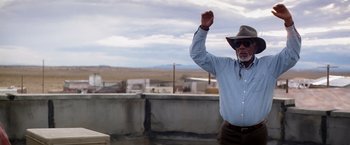 Movie still from “Transcendence” (2014), directed by Wally Pfister – An older man wearing a cowboy hat raises his fist in the air; Medium shot, Low angle