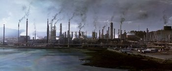 Movie still from “Transcendence” (2014), directed by Wally Pfister – An oil refinery with smoke coming out of its stacks; Extreme Wide shot, High angle
