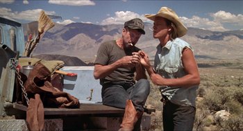 Movie still from “Tremors” (1990), directed by Ron Underwood – A man and a woman sitting on a bench in the desert; Medium shot, Low angle