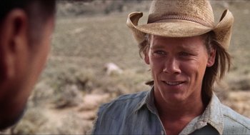 Movie still from “Tremors” (1990), directed by Ron Underwood – A man wearing a cowboy hat in a field; Close Up shot, Over the shoulder angle