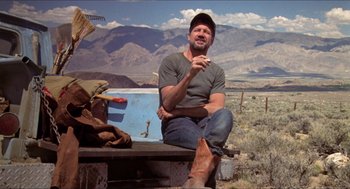 Movie still from “Tremors” (1990), directed by Ron Underwood – A man sitting on top of a wooden bench in the desert; Wide shot, Low angle