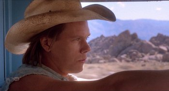 Movie still from “Tremors” (1990), directed by Ron Underwood – A man wearing a cowboy hat looking out a window; Close Up shot, Low angle