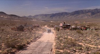Movie still from “Tremors” (1990), directed by Ron Underwood – A car driving down a dirt road in the middle of the desert; Extreme Wide shot, High angle