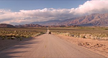 Movie still from “Tremors” (1990), directed by Ron Underwood – A car driving down the middle of a road; Extreme Wide shot, High angle