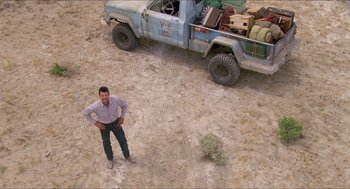 Movie still from “Tremors” (1990), directed by Ron Underwood – A man standing in front of a blue truck; Extreme Wide shot, Overhead angle