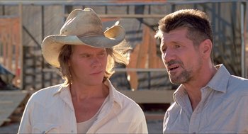 Movie still from “Tremors” (1990), directed by Ron Underwood – A man wearing a cowboy hat talking to another man; Close Up shot, Low angle