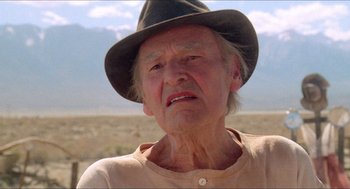 Movie still from “Tremors” (1990), directed by Ron Underwood – An old man wearing a black hat and a beige shirt; Close Up shot, Low angle