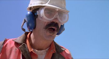 Movie still from “Tremors” (1990), directed by Ron Underwood – A man wearing a hard hat and ear muffs; Close Up shot, Low angle