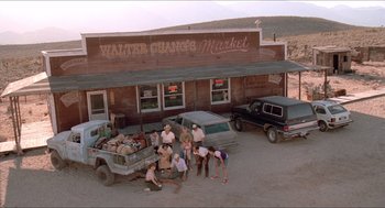 Movie still from “Tremors” (1990), directed by Ron Underwood – A group of people standing around a truck in front of a market; Extreme Wide shot, High angle