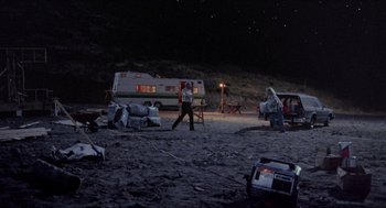 Movie still from “Tremors” (1990), directed by Ron Underwood – A couple of people standing on top of a sandy beach; Extreme Wide shot, High angle