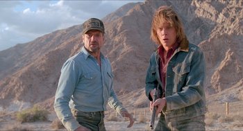Movie still from “Tremors” (1990), directed by Ron Underwood – A man and a boy standing next to each other holding guns; Medium shot, Low angle
