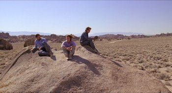 Movie still from “Tremors” (1990), directed by Ron Underwood – A group of people sitting on top of a hill; Wide shot, High angle