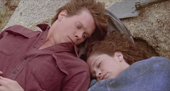 Movie still from “Tremors” (1990), directed by Ron Underwood – Two people laying on the ground with their eyes closed; Close Up shot, Overhead angle