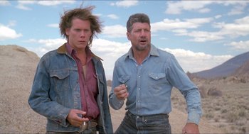 Movie still from “Tremors” (1990), directed by Ron Underwood – A man and a woman standing next to each other in the desert; Medium shot, Low angle