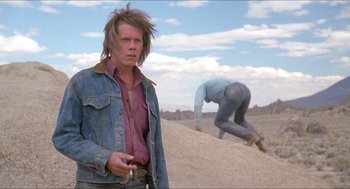 Movie still from “Tremors” (1990), directed by Ron Underwood – A man standing in the sand with a cigarette in his mouth; Medium shot, Low angle