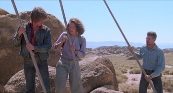 Movie still from “Tremors” (1990), directed by Ron Underwood – Two people standing next to each other on a rocky hillside; Wide shot, Low angle