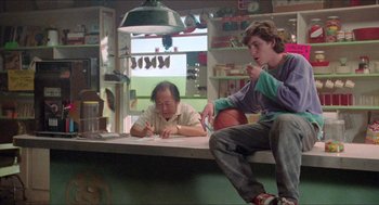 Movie still from “Tremors” (1990), directed by Ron Underwood – Two people sitting on a bench in a room; Wide shot, Low angle