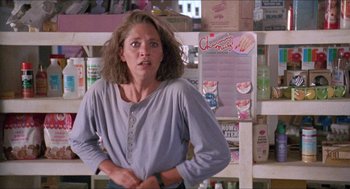 Movie still from “Tremors” (1990), directed by Ron Underwood – A woman standing in front of a wall with a bunch of boxes; Medium shot, Over the shoulder angle