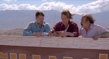 Movie still from “Tremors” (1990), directed by Ron Underwood – A group of people sitting on top of a wooden deck; Wide shot, Low angle