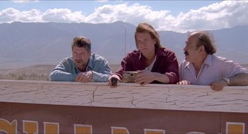 Movie still from “Tremors” (1990), directed by Ron Underwood – Three men are sitting on a balcony and one is holding a cell phone; Medium shot, Low angle