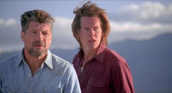 Movie still from “Tremors” (1990), directed by Ron Underwood – Two men standing next to each other in front of a sky background; Close Up shot, Low angle