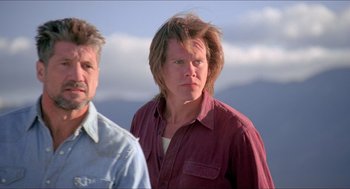 Movie still from “Tremors” (1990), directed by Ron Underwood – A man standing next to another man in front of a sky background; Close Up shot, Low angle