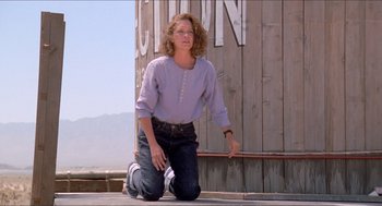 Movie still from “Tremors” (1990), directed by Ron Underwood – A woman kneeling on the ground in front of a building; Wide shot, Low angle