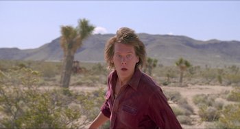 Movie still from “Tremors” (1990), directed by Ron Underwood – A man in a red shirt is in the middle of the desert; Close Up shot, Low angle