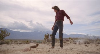 Movie still from “Tremors” (1990), directed by Ron Underwood – A man standing in the sand next to an animal; Wide shot, Low angle