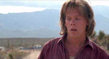 Movie still from “Tremors” (1990), directed by Ron Underwood – A man with long brown hair is standing in the desert; Close Up shot, Over the shoulder angle